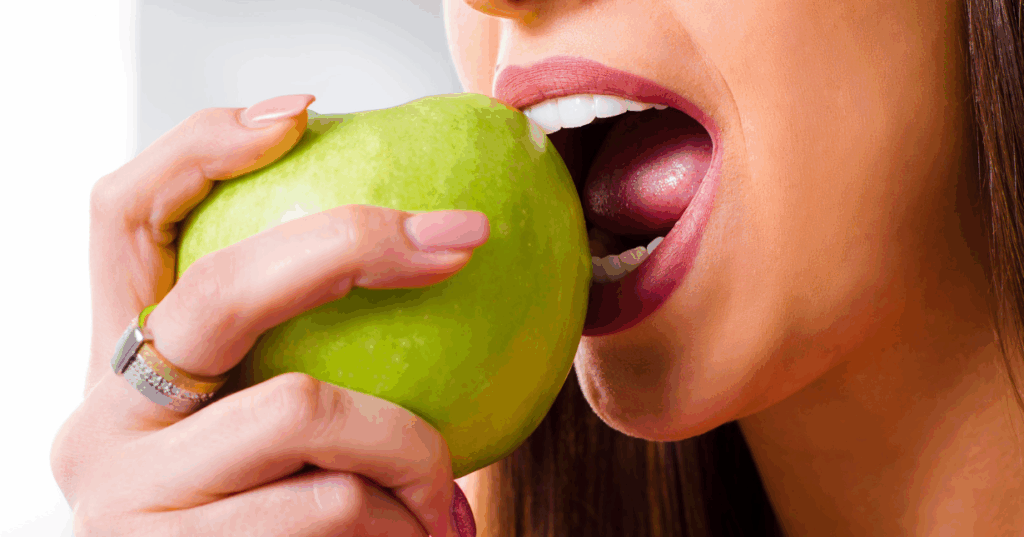 Close-up of a woman confidently biting into a green apple, showcasing strong, healthy teeth.