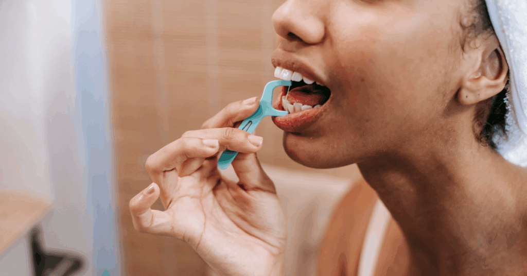 Woman flossing her teeth with a turquoise dental flosser in a bathroom setting