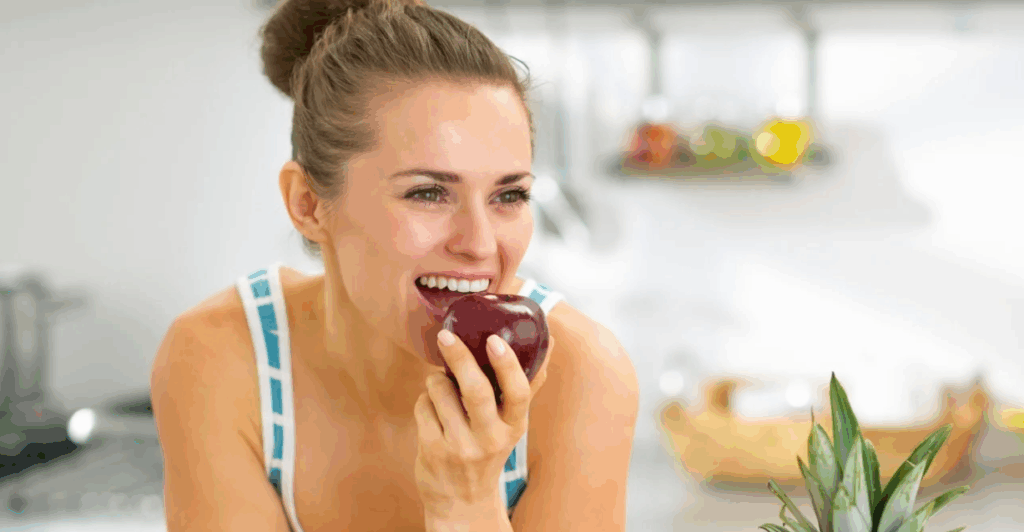 Smiling woman confidently bites into a red apple—showcasing the natural strength and comfort of a single tooth implant.