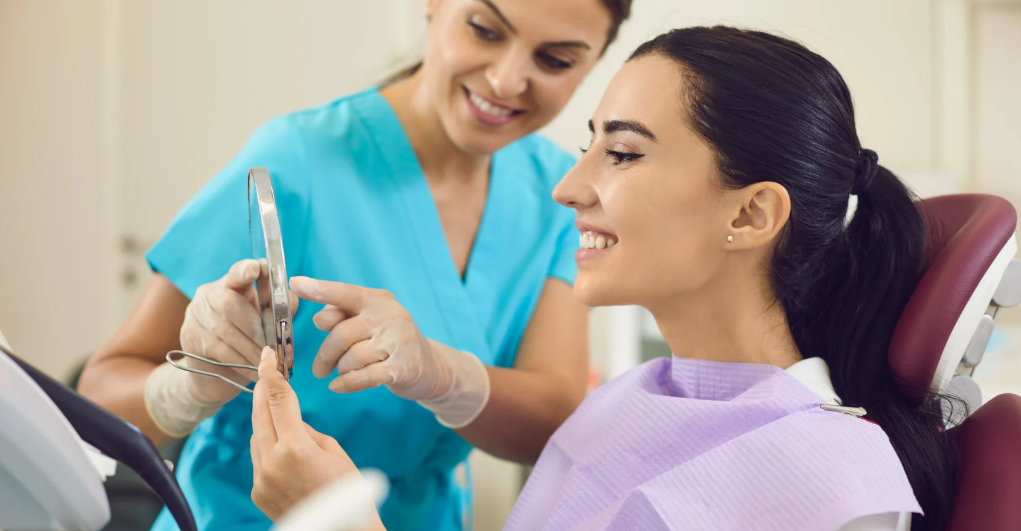 Female dentist showing a happy patient her smile in a handheld mirror during a consultation in a dental office.